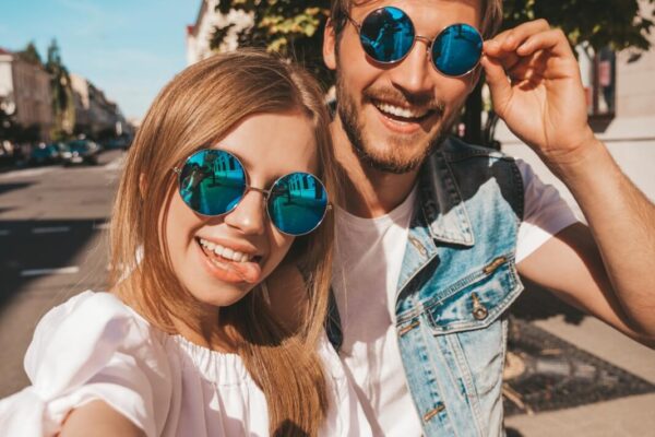 Para uśmiecha się w słońcu, nosząc modne okulary przeciwsłoneczne.