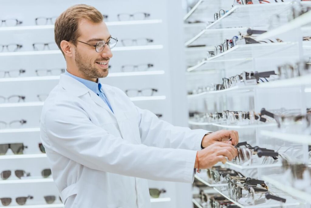 Optyk NFZ w białym fartuchu wybiera okulary z półki.