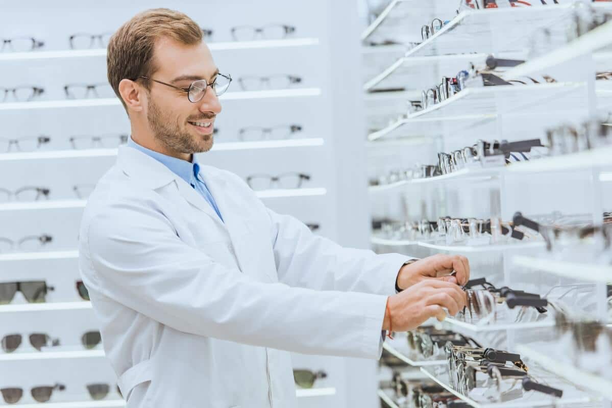 Optyk NFZ w białym fartuchu wybiera okulary z półki.