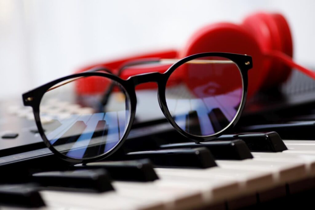 Okulary progresywne leżą na klawiaturze pianina obok czerwonych słuchawek.