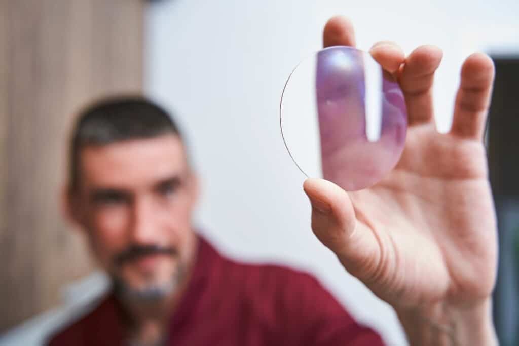 Mężczyzna trzyma szkła progresywne między palcami, oglądając je z bliska.
