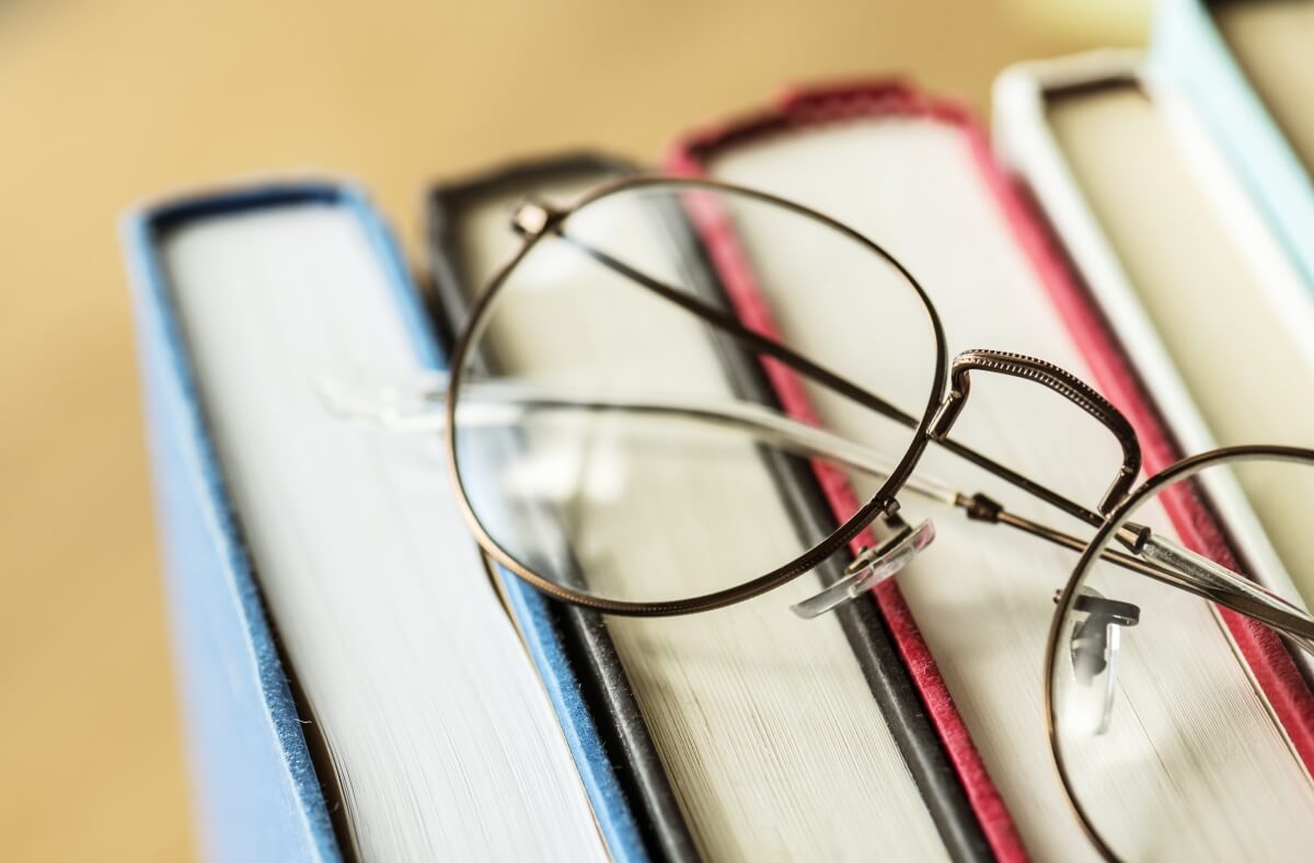 Okulary z cienkimi oprawkami leżą na stosie książek, a ich szkła okularowe są dobrze widoczne.