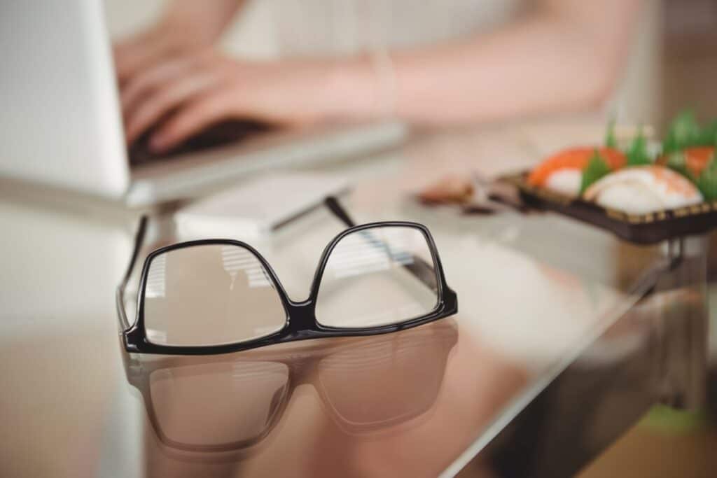 Na stole leżą okulary, których soczewki okularowe odbijają światło.